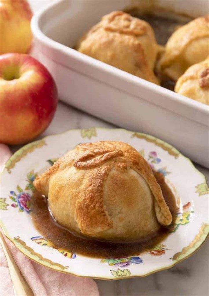 Two apple dumplings on a white plate topped with ice cream.